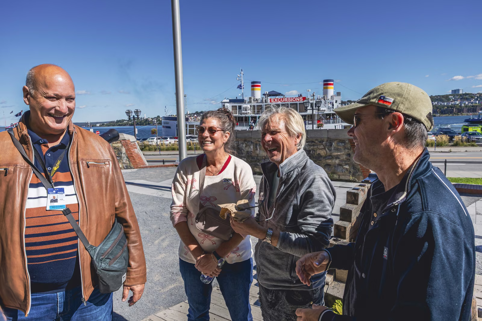A Tours Voir Québec guide sharing a laugh with visitors in the Lower Town, the St. Lawrence River and a ferry behind them.